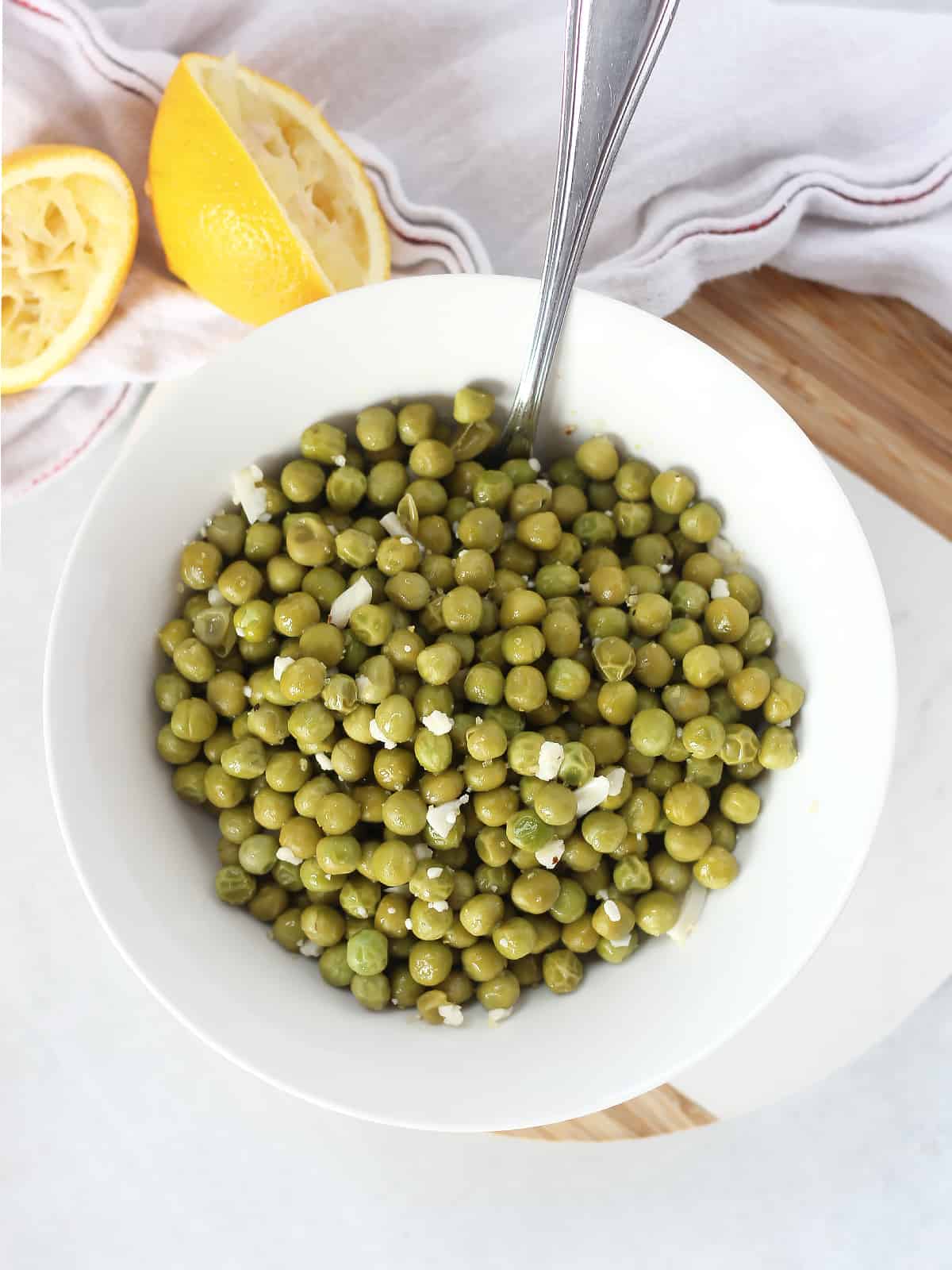 Green peas in a bowl with a spoon, next to squeezed lemon halves.