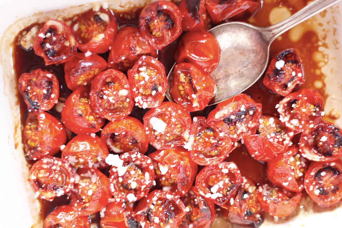 Close up of roasted cherry tomatoes in a baking dish with a spoon.