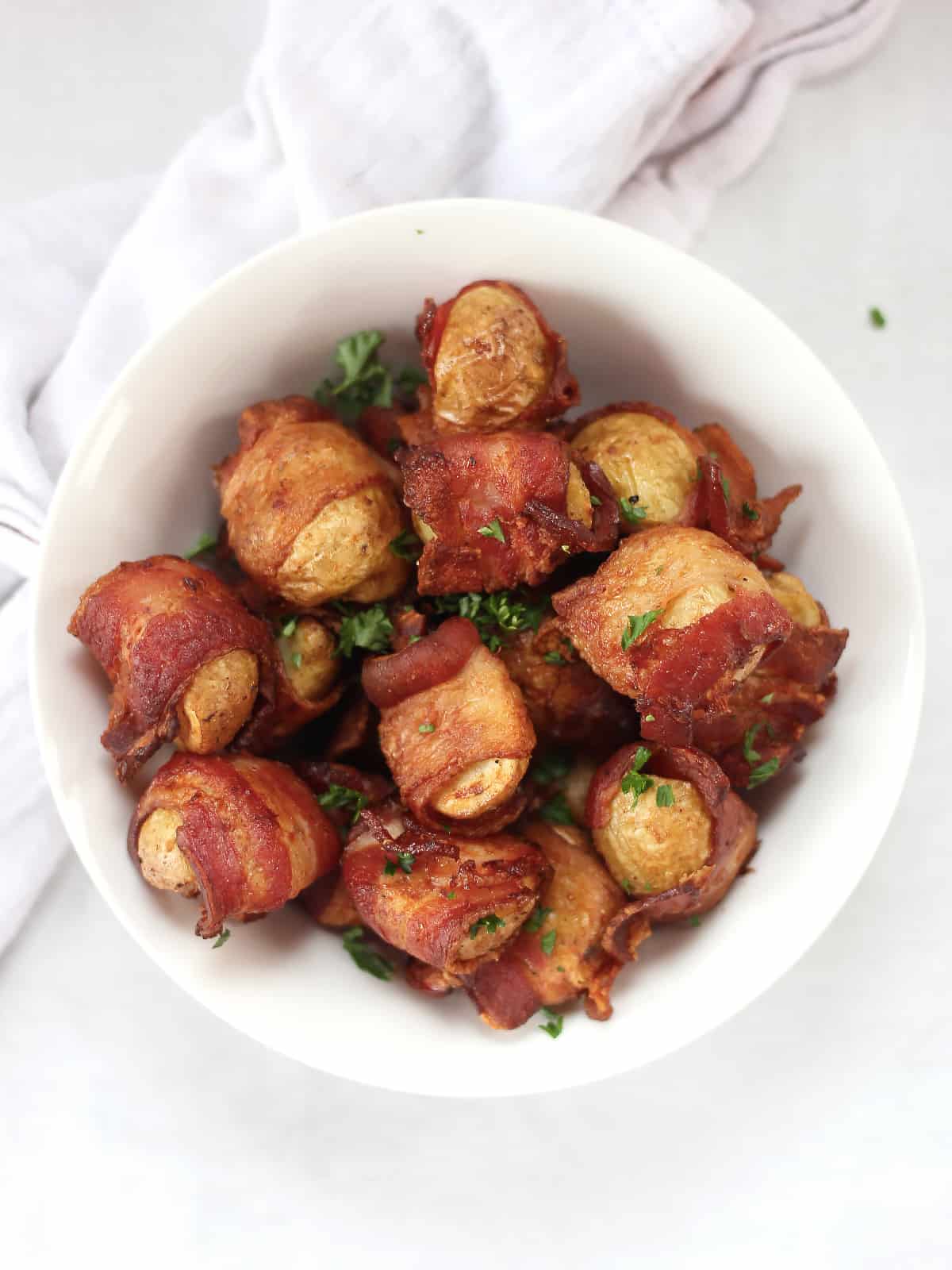 Air fried bacon wrapped potatoes in a serving bowl and garnished with parsley.