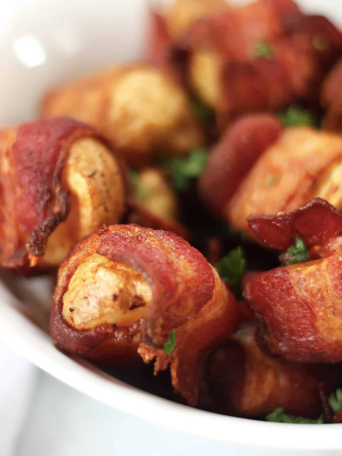 Close up of baby potatoes wrapped in bacon in a white bowl.