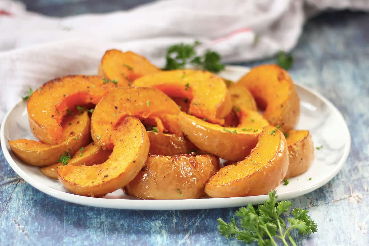 Sliced roasted butterkin squash on a plate with fresh herb garnish.