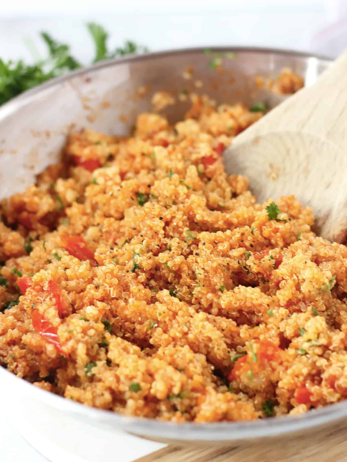 A wooden spoon stirring the quinoa and tomatoes in a skillet.