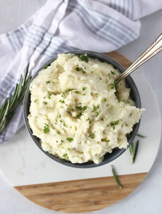 Mashed potatoes in a bowl garnished with fresh herbs.