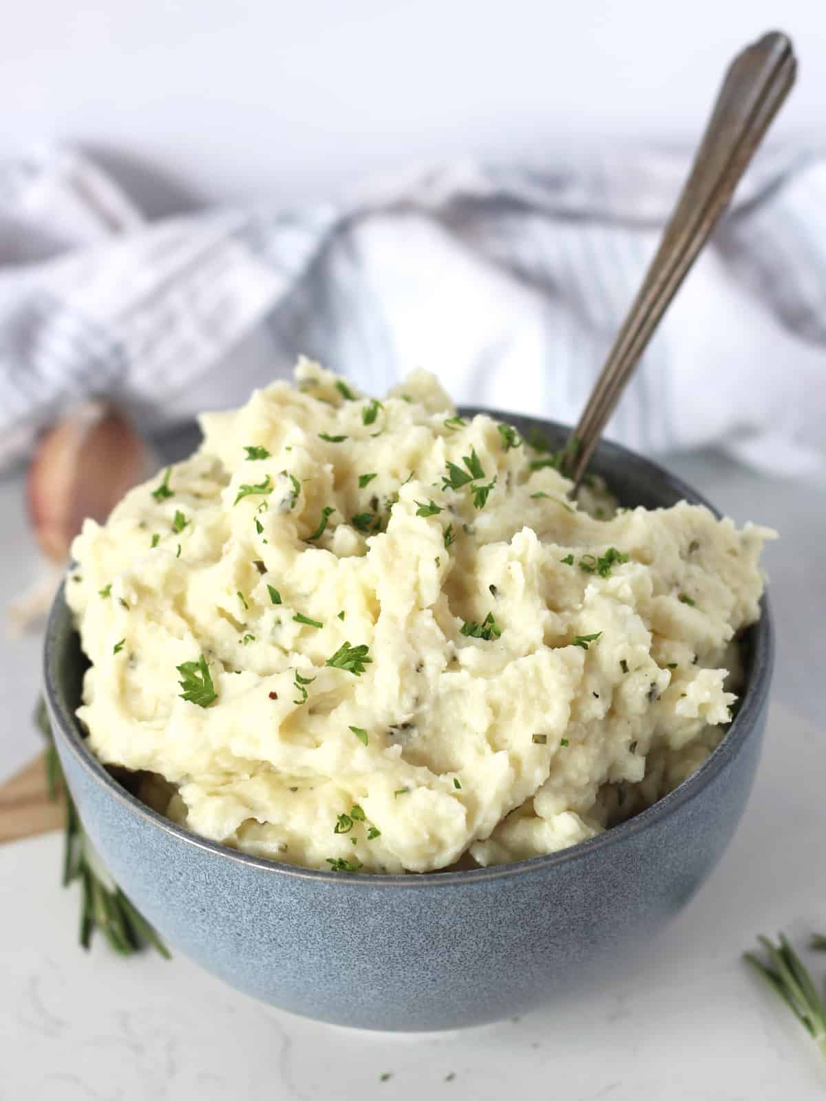 Rosemary garlic mashed potatoes in a blue bowl with a spoon.