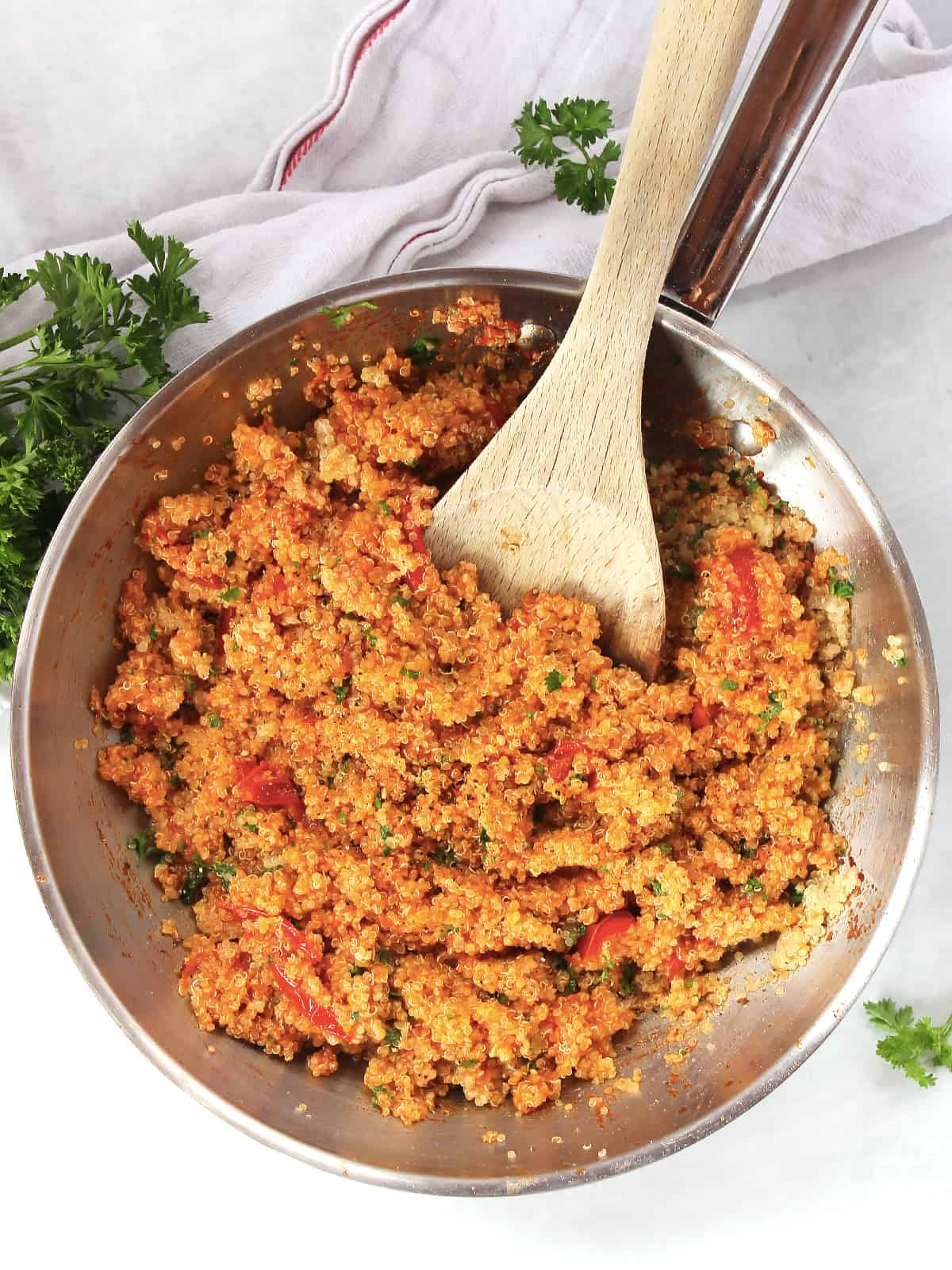Tomato quinoa in a silver skillet with a wooden spoon.