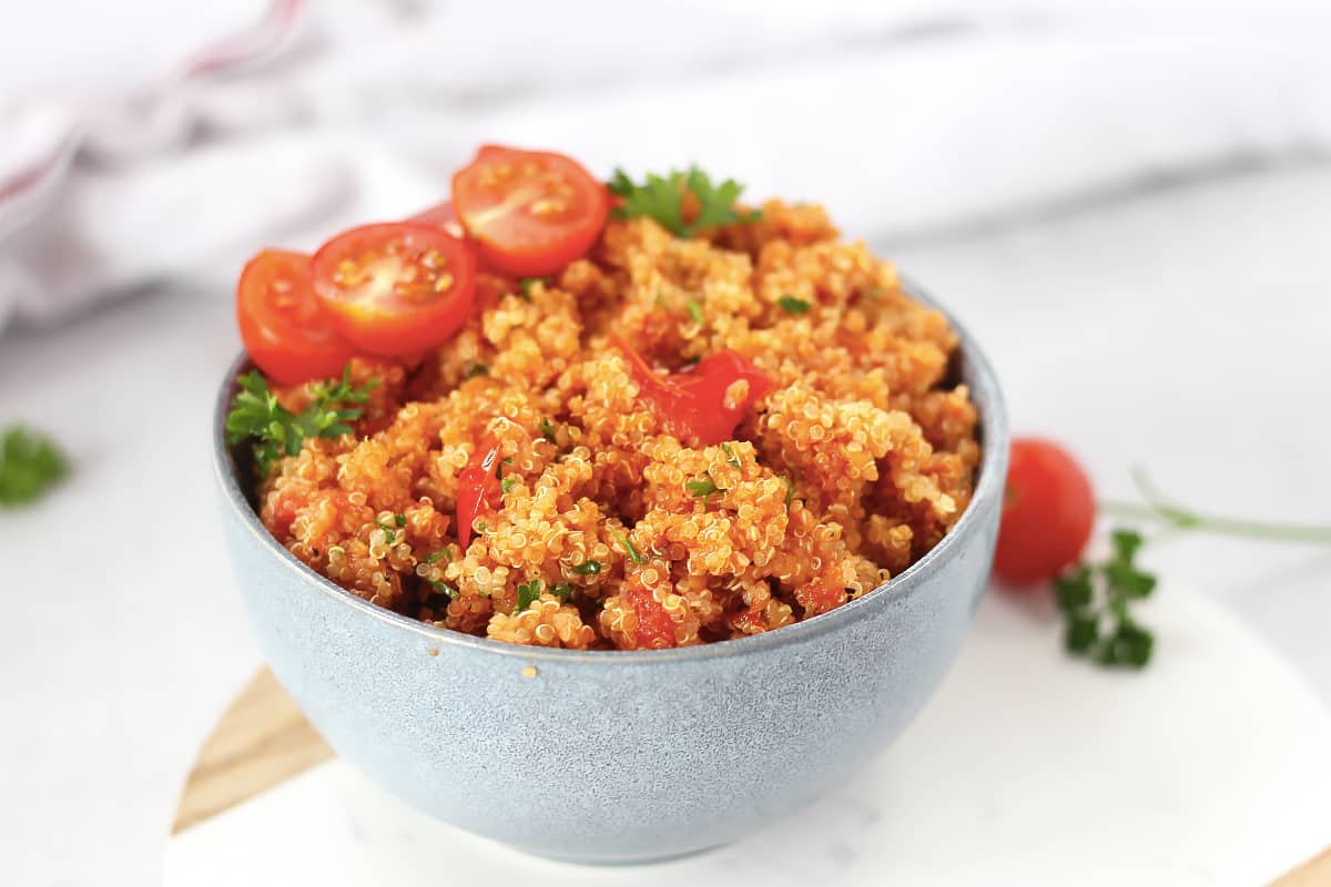 Tomato quinoa served in a blue bowl with fresh cherry tomatoes and parsley.