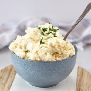 Cheese mash with garlic in a bowl with a spoon and garnished with fresh herbs.