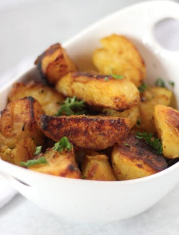 Golden brown roasted potatoes in a white bowl garnished with fresh parsley.