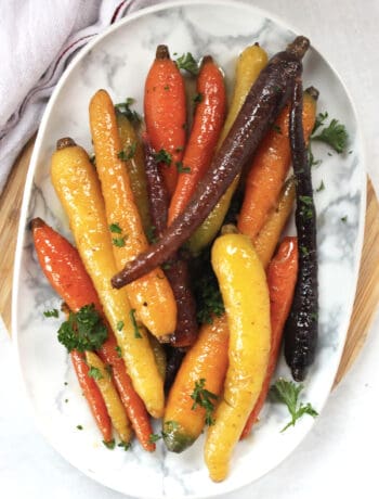 Maple ginger carrots arranged on a serving plate and garnished with fresh herbs.
