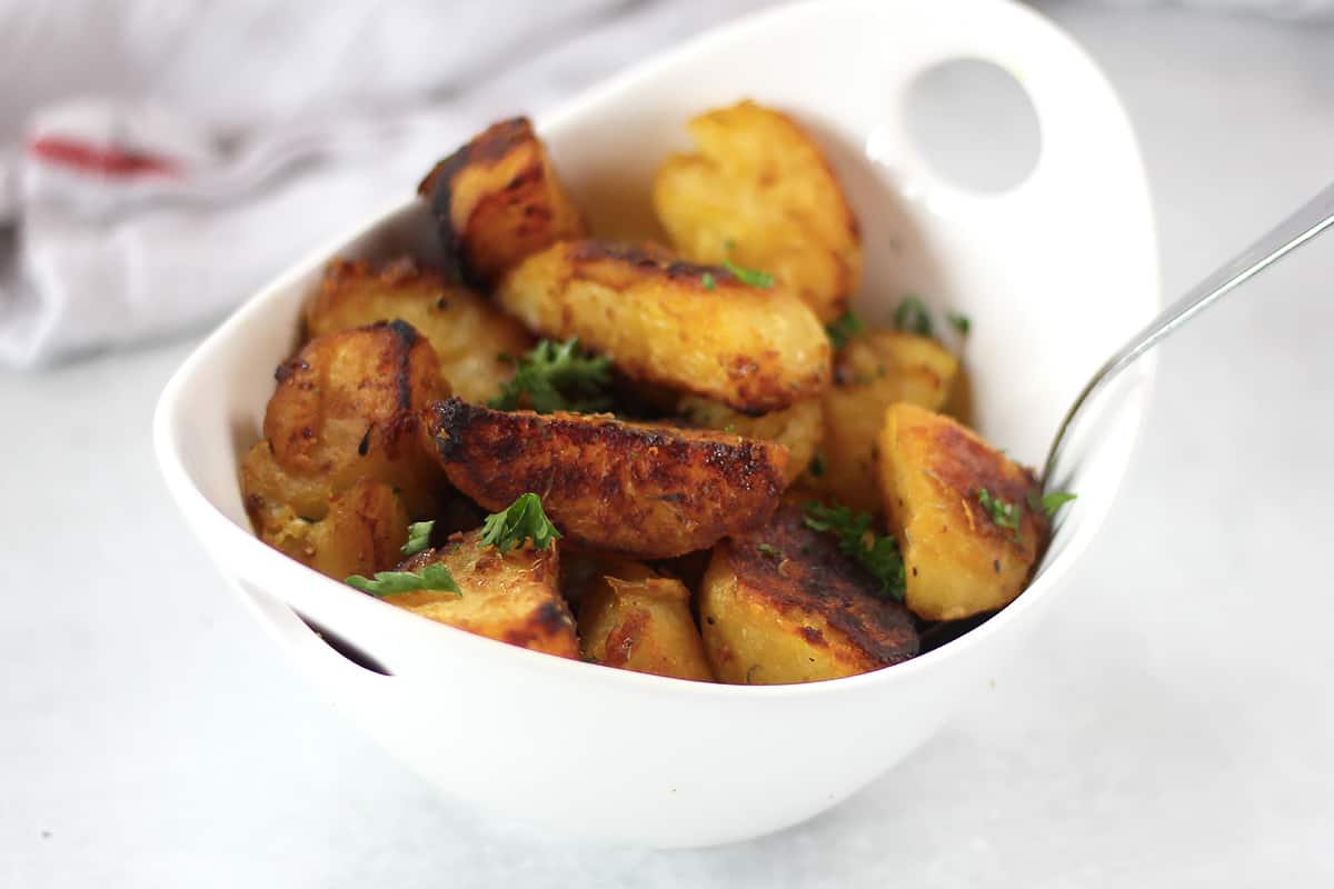 Crispy roasted potatoes in a bowl with a serving spoon.
