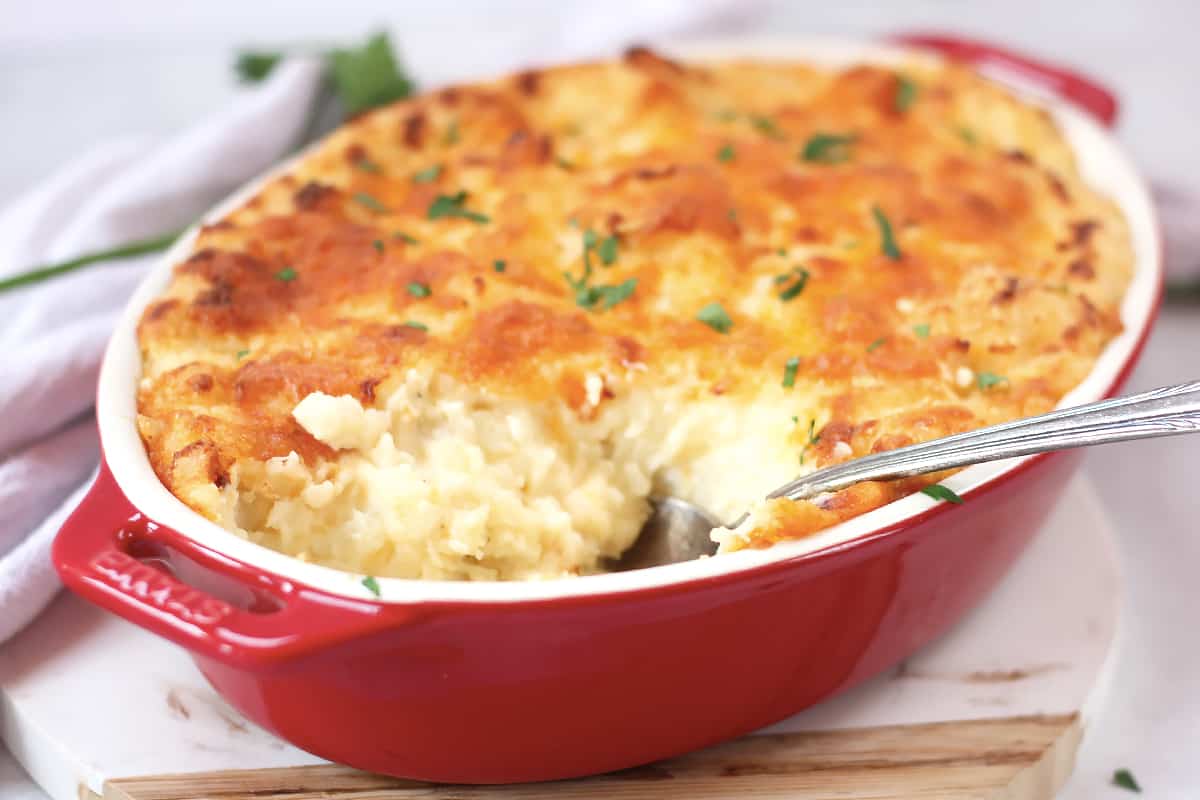 Twice baked mashed potato in a red casserole dish with a serving spoon.
