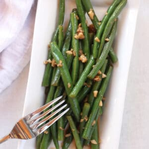 Sautéed green beans cooked in balsamic vinegar on a white plate.