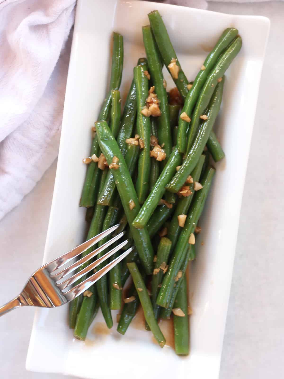 Balsamic green beans served on a white oblong plate with a fork.