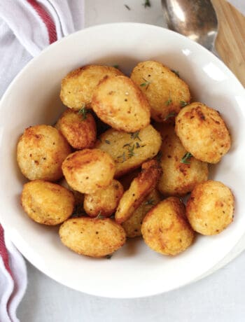 Roasted canned potatoes in a white bowl garnished with fresh herbs.