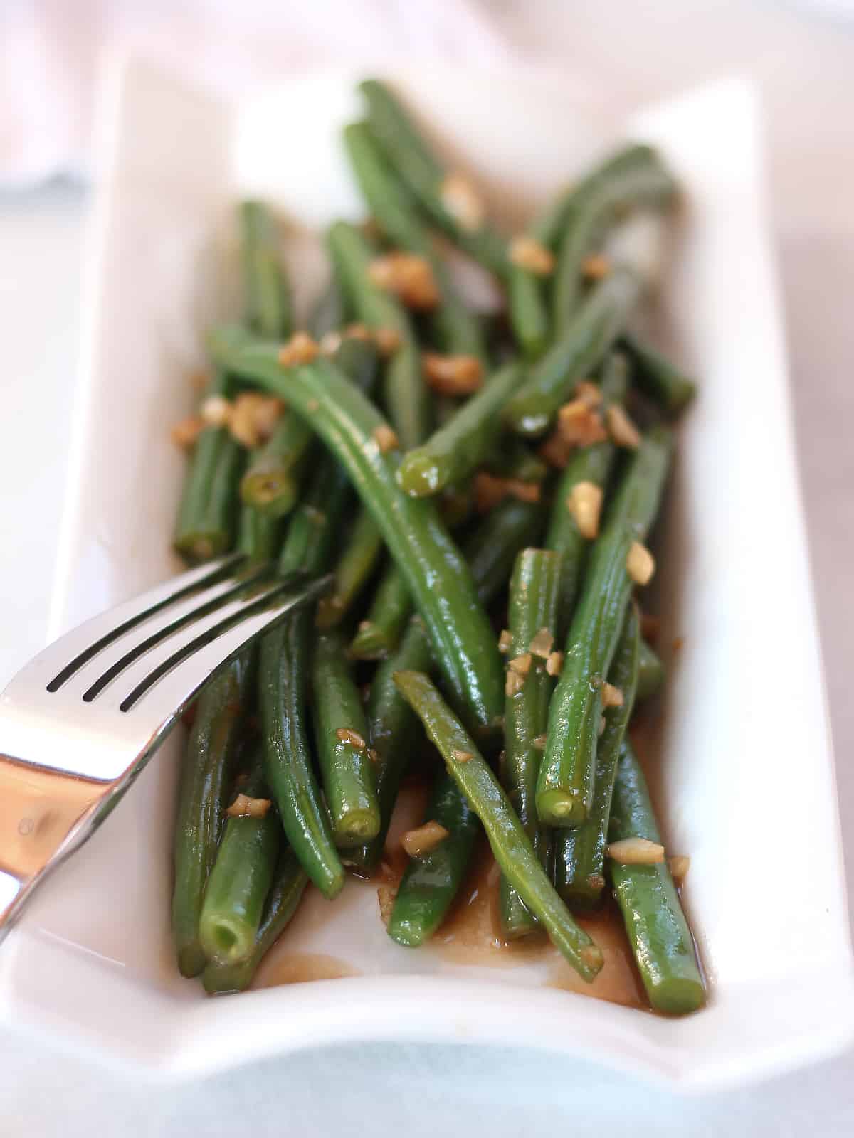 Green beans cooked with balsamic and garlic served in a white plate with a fork.