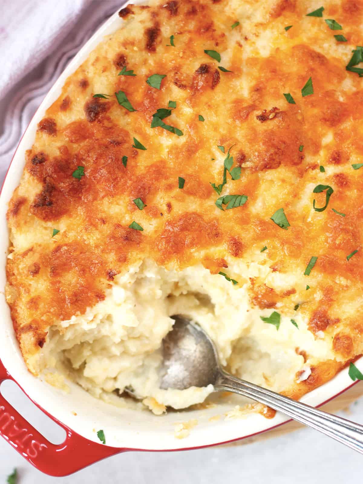 A spoon in a twice baked mashed potato casserole topped with cheese.