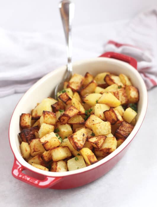 Air fryer diced potatoes piled into a serving dish with a silver spoon.