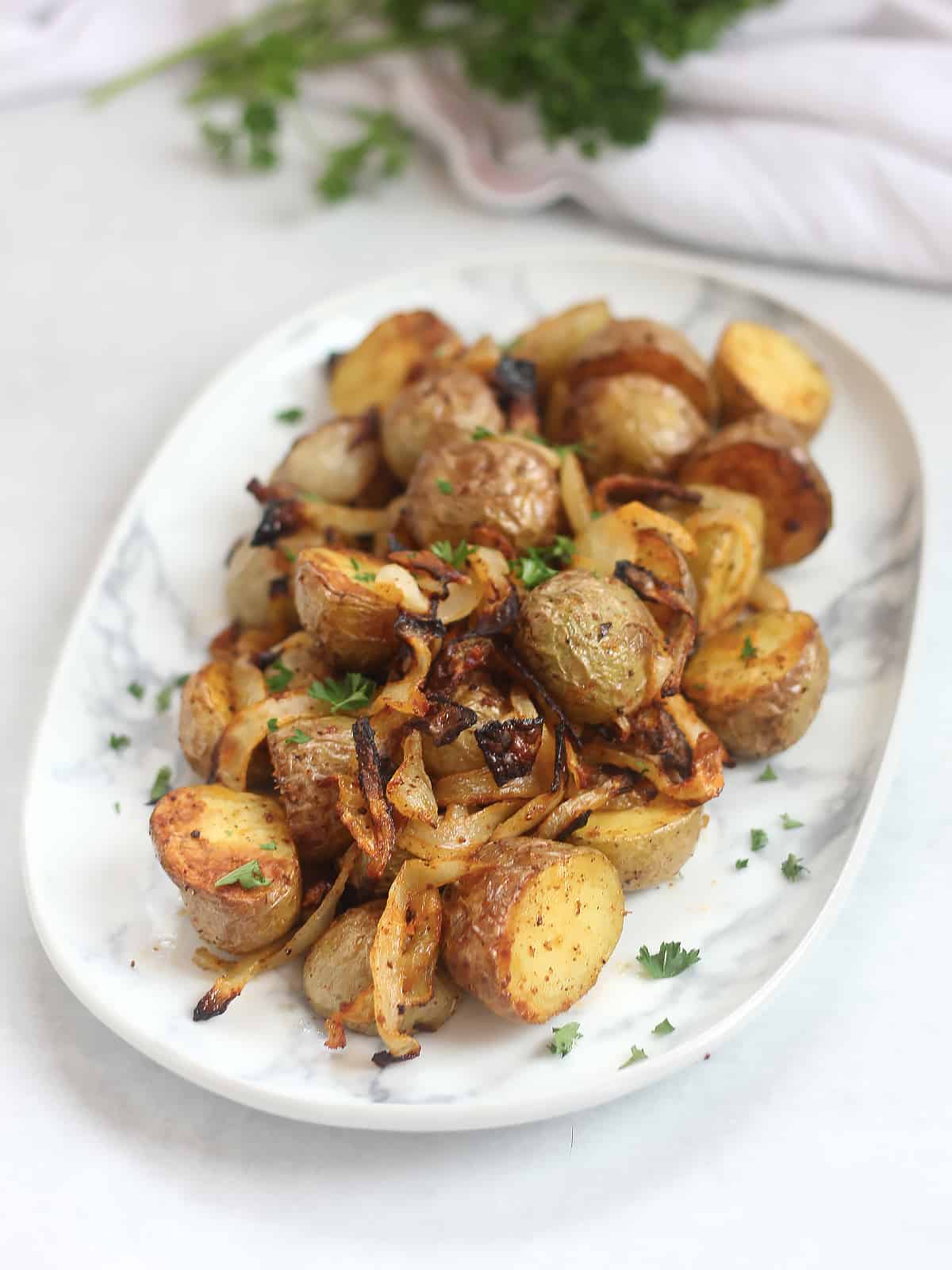 Air fried baby potatoes and onions on a plate garnished with fresh parsley.