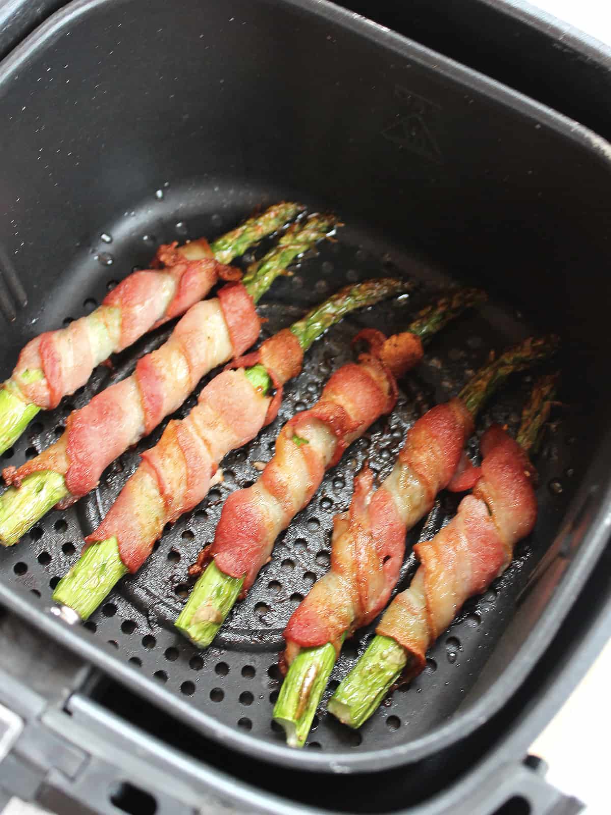 Bacon wrapped asparagus in an air fryer basket.