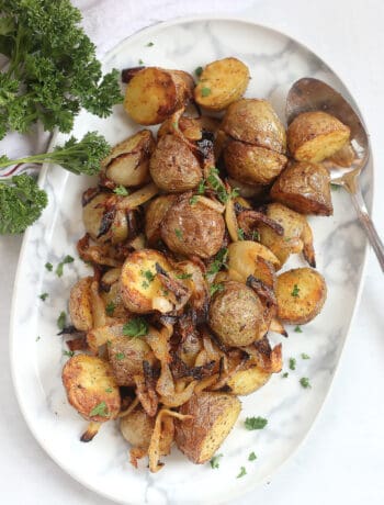 Air fryer potatoes and onions on a serving plate with a spoon.