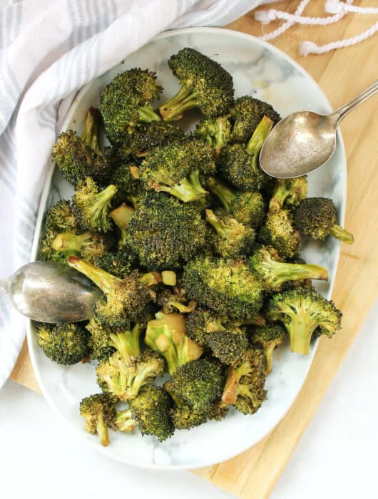 Roasted balsamic broccoli florets on a plate with two serving spoons.