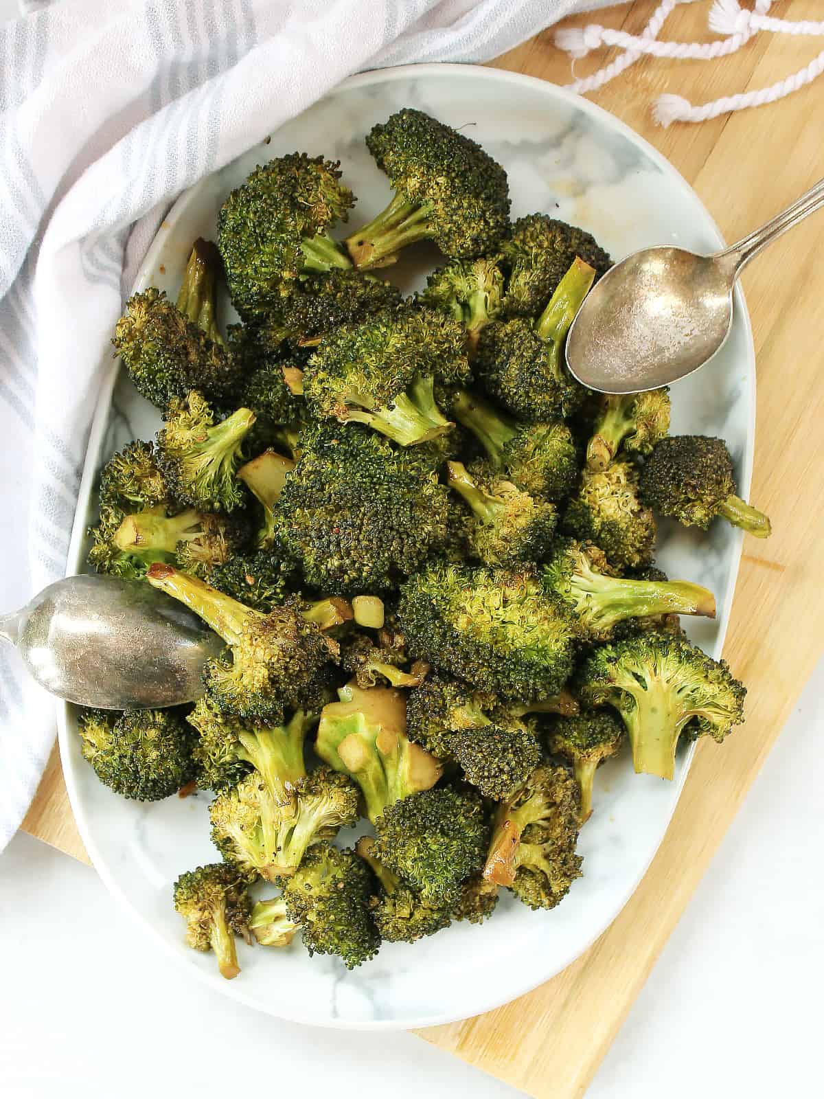 Roasted balsamic broccoli florets on a plate with two serving spoons.