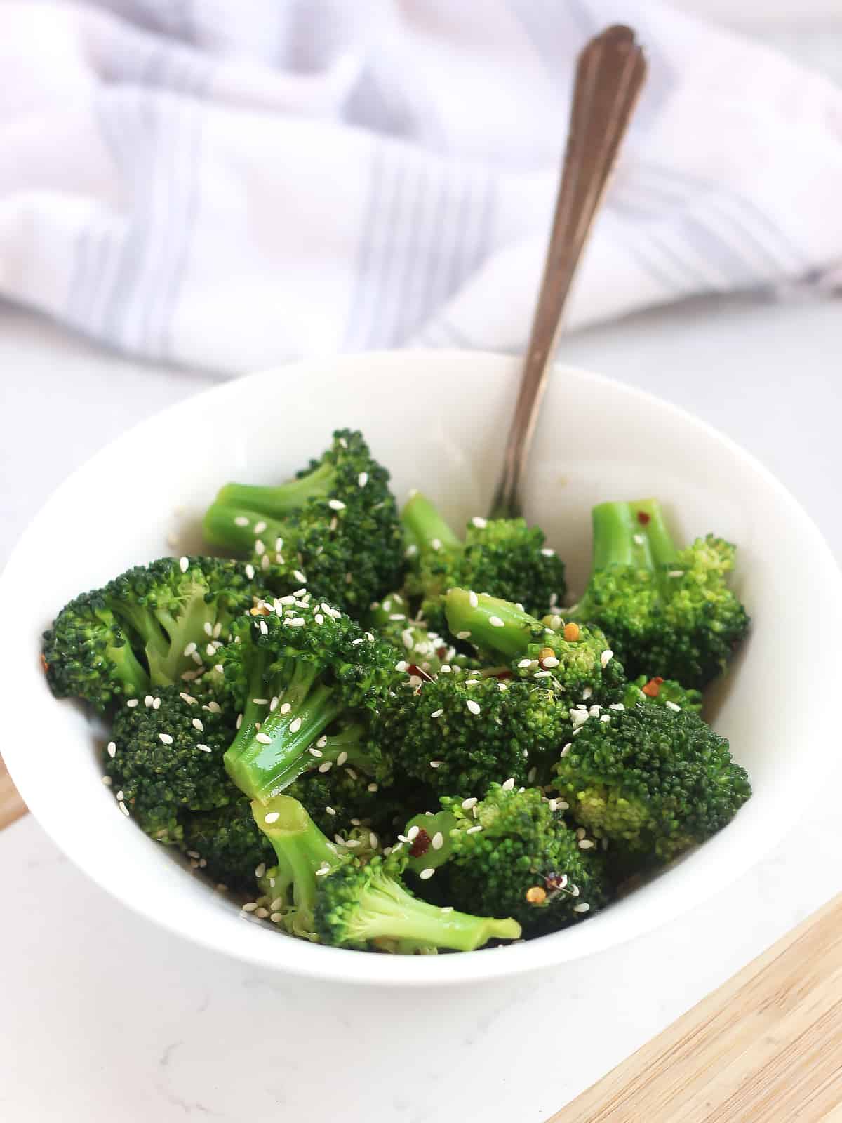 Cooked broccoli topped with sesame seeds in a white bowl.