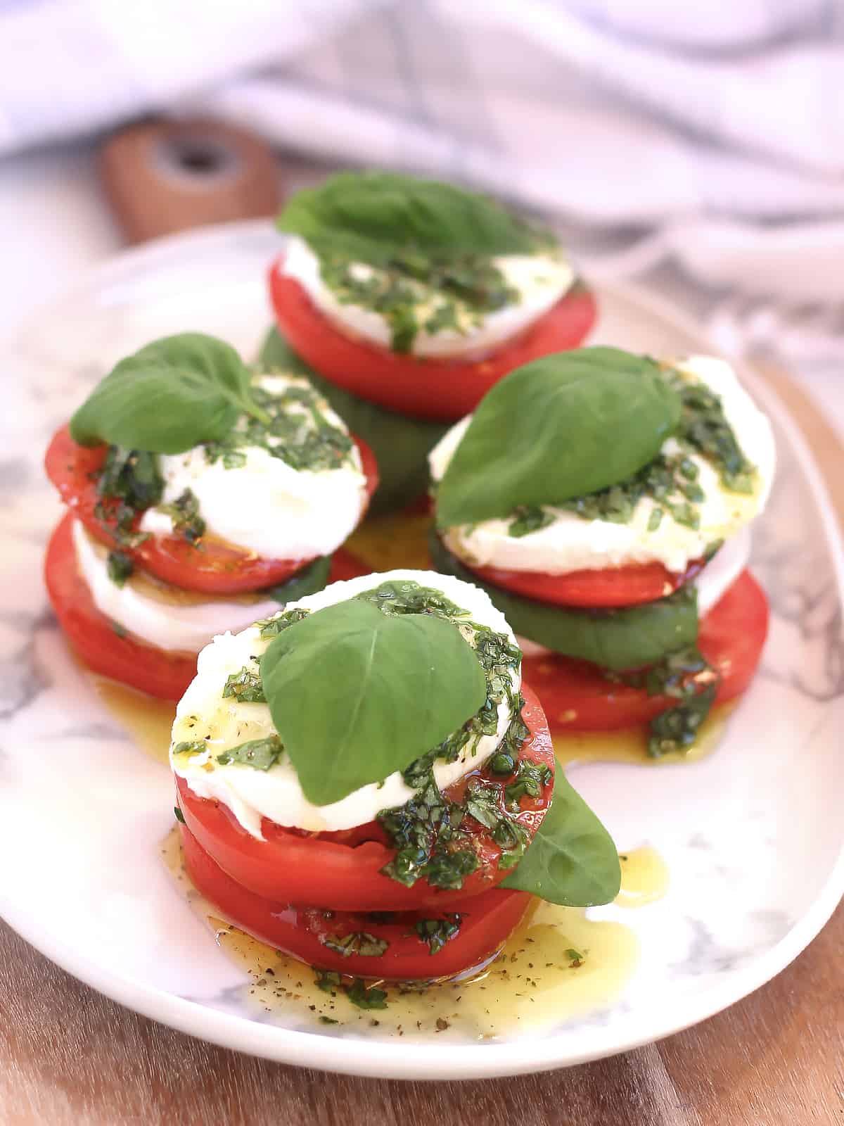 Four caprese salad stacks on a serving plate.