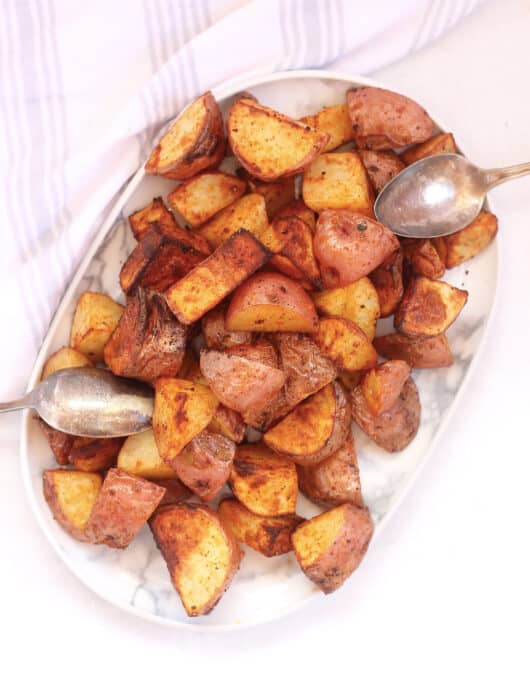 Air fryer roasted red skinned potatoes on a serving plate with two spoons.