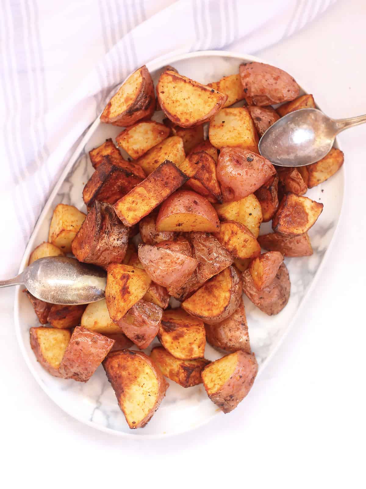 Air fryer roasted red skinned potatoes on a serving plate with two spoons.