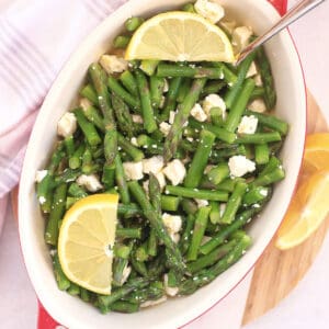 Asparagus and feta tossed in a lemon dressing served in a dish with a spoon.