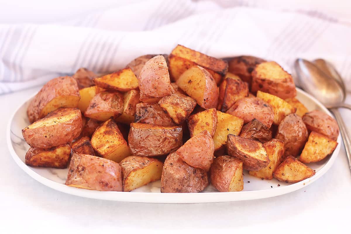Air fried red skinned potatoes on a serving plate next to two spoons.