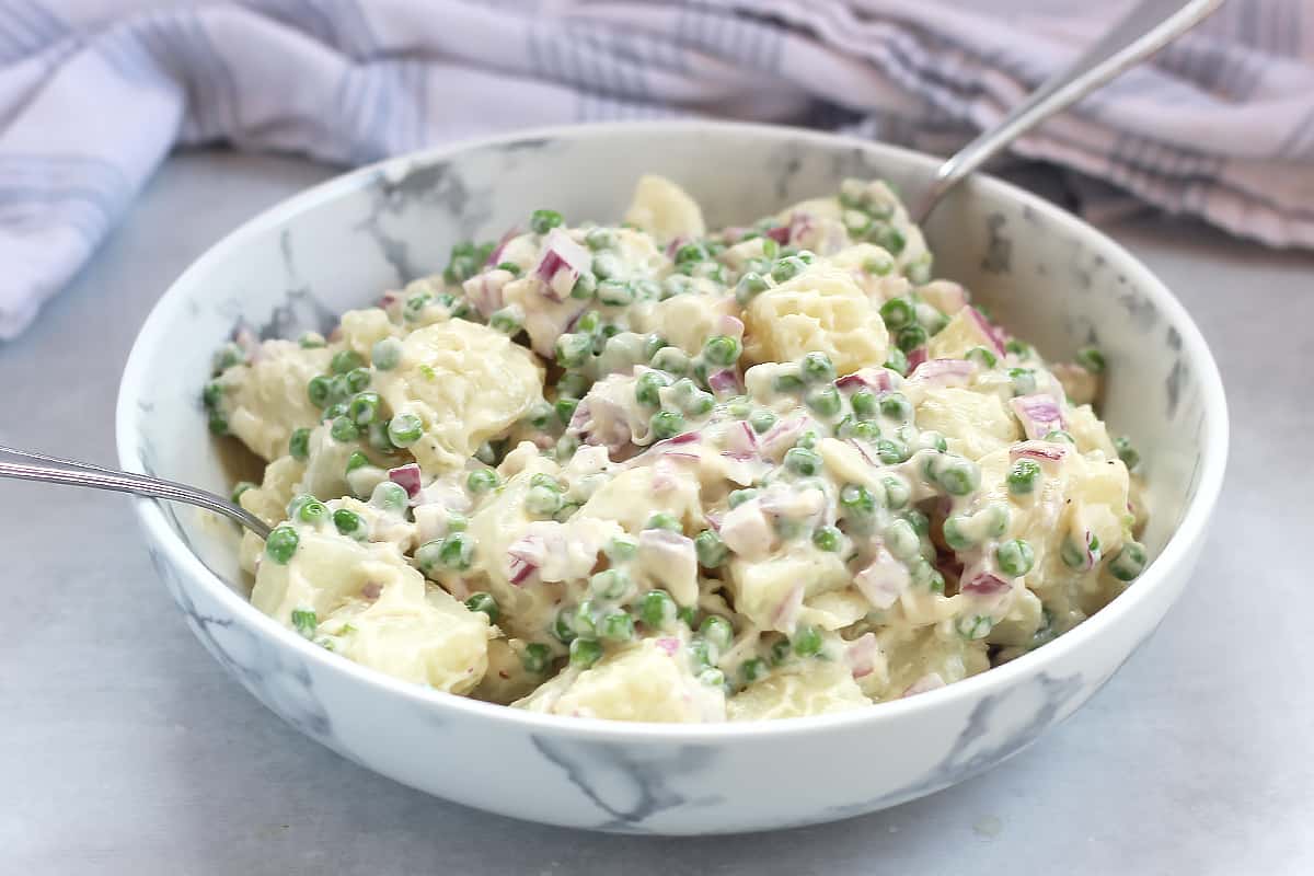 Creamy potato salad with peas and red onion in a serving bowl with two spoons.