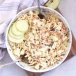 Two serving spoons in a bowl of cabbage and apple slaw.