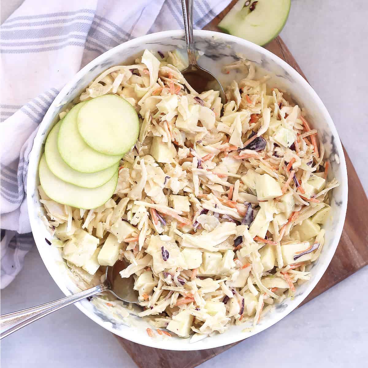 Two serving spoons in a bowl of cabbage and apple slaw.