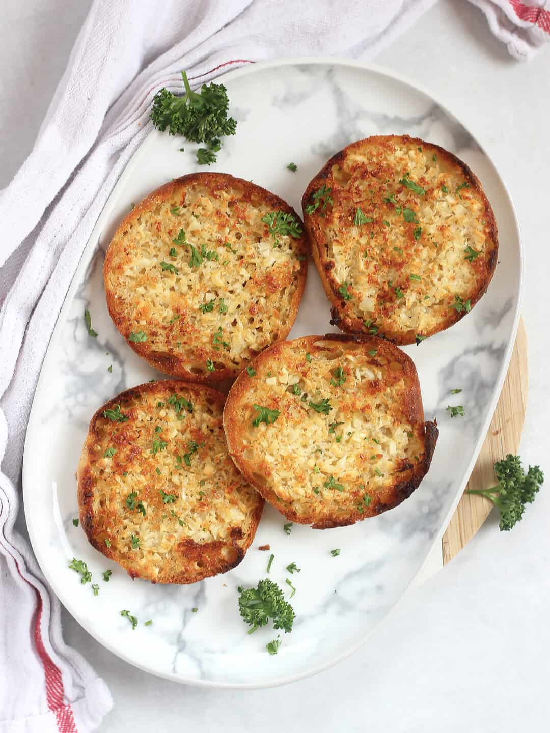 Baked garlic bread English muffins on a plate with fresh parsley garnish.