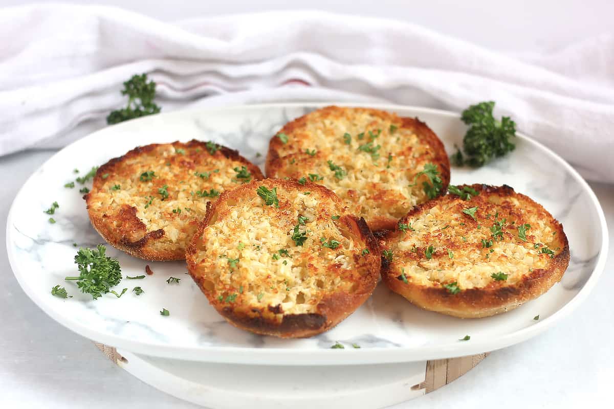 Garlic English muffin halves on a white plate.