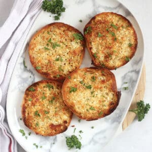 Four garlic bread English muffin halves on a serving plate.