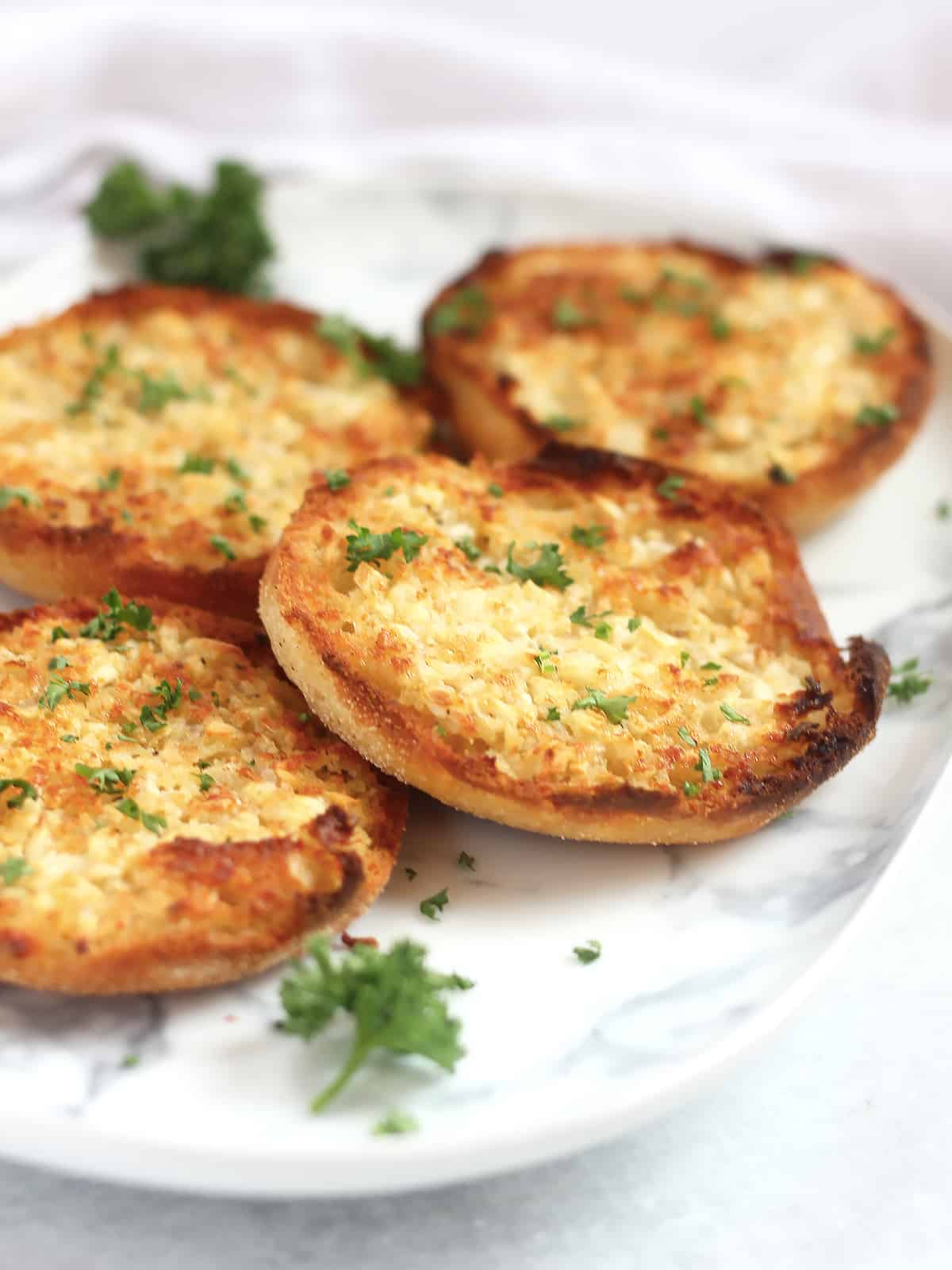 Golden brown garlic bread English muffins garnished with fresh parsley.