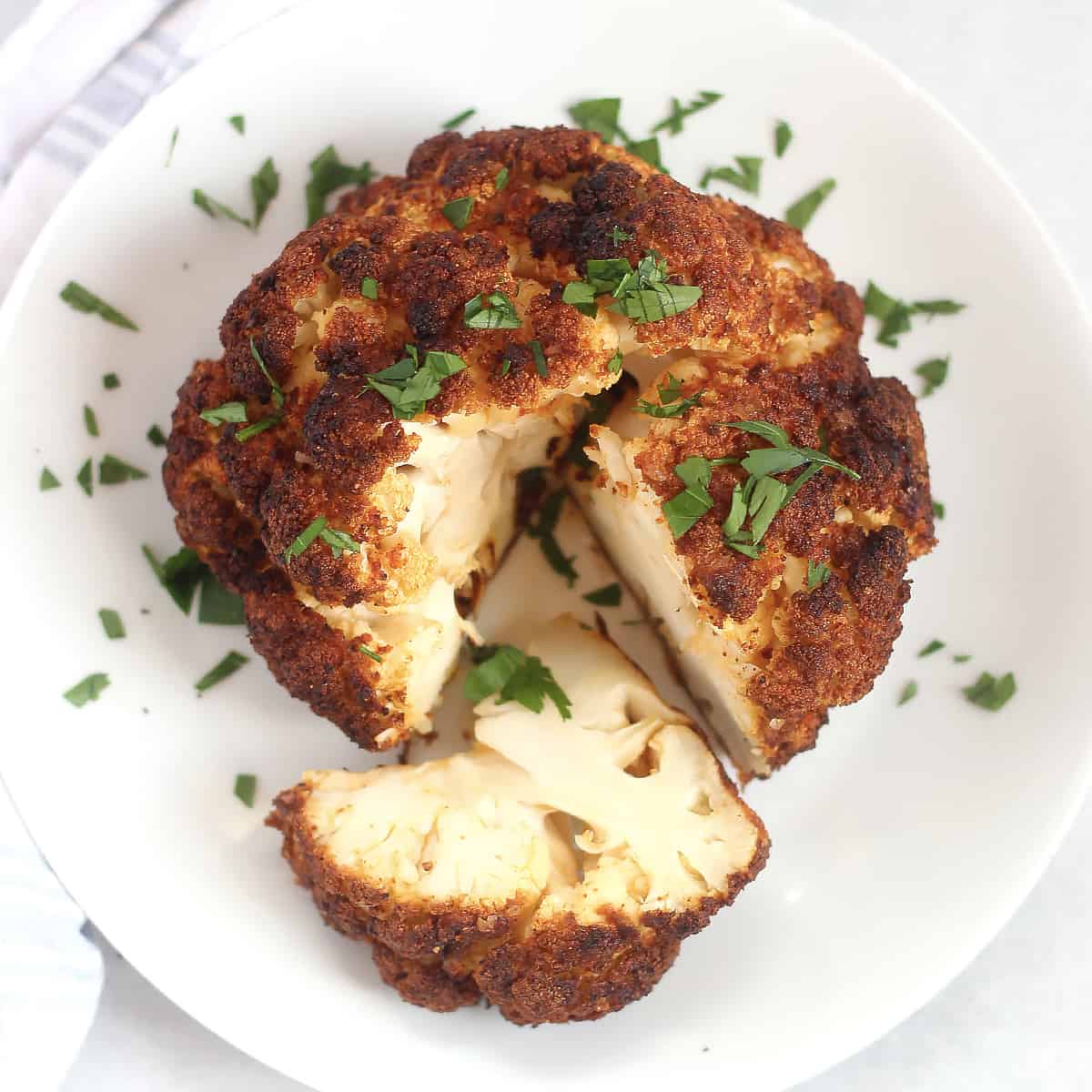 An air fryer whole roasted cauliflower served on a white plate with a slice cut out of it.