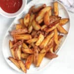 Golden brown red skinned fries on a plate next to a dipping sauce.