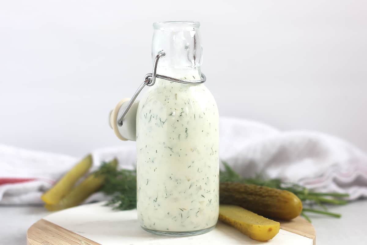 Salad dressing with dill and pickles in a glass bottle.