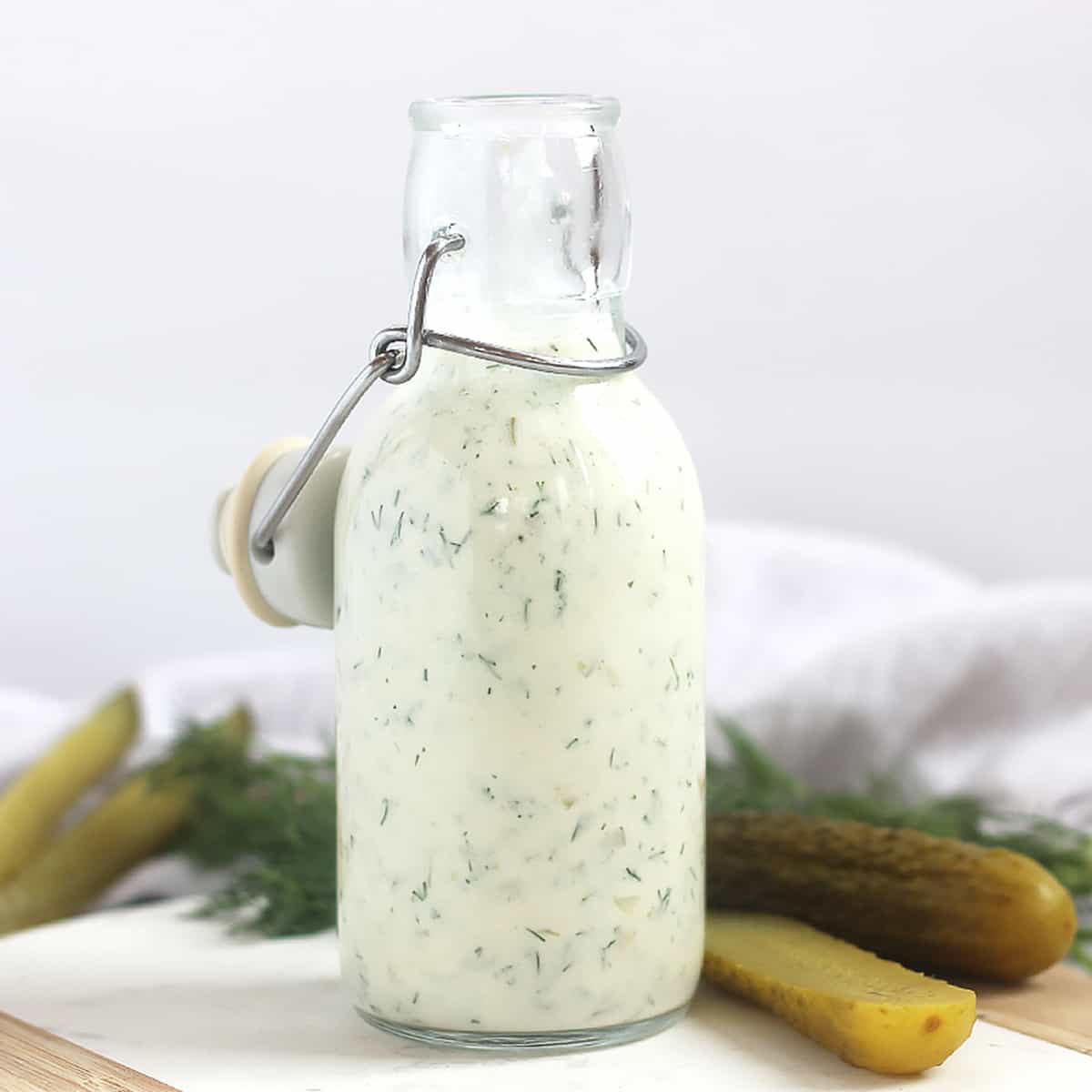 Creamy salad dressing next to fresh dill and cut pickles.