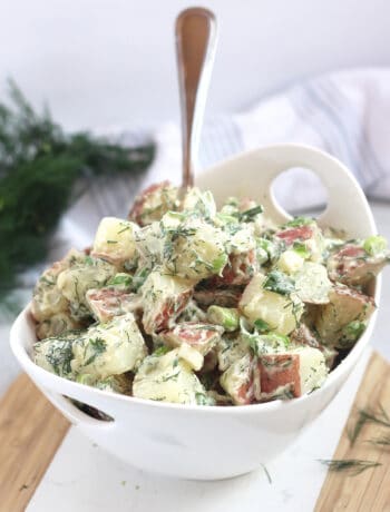 Red skinned potatoes tossed in a creamy dill dressing and served in a white bowl.