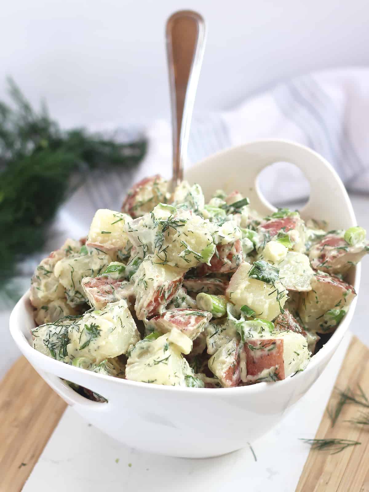 Red skinned potatoes tossed in a creamy dill dressing and served in a white bowl.
