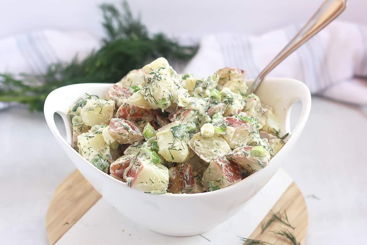 A spoon in a bowl of creamy red skin potato salad.