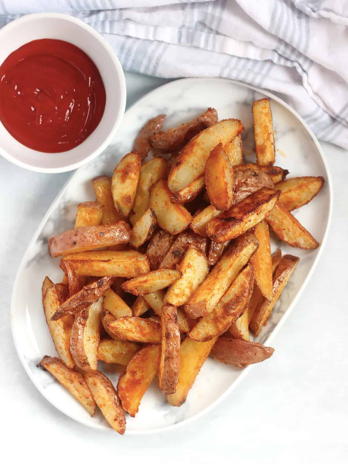 Red skinned potato fries served on a plate next to a pot of tomato ketchup.
