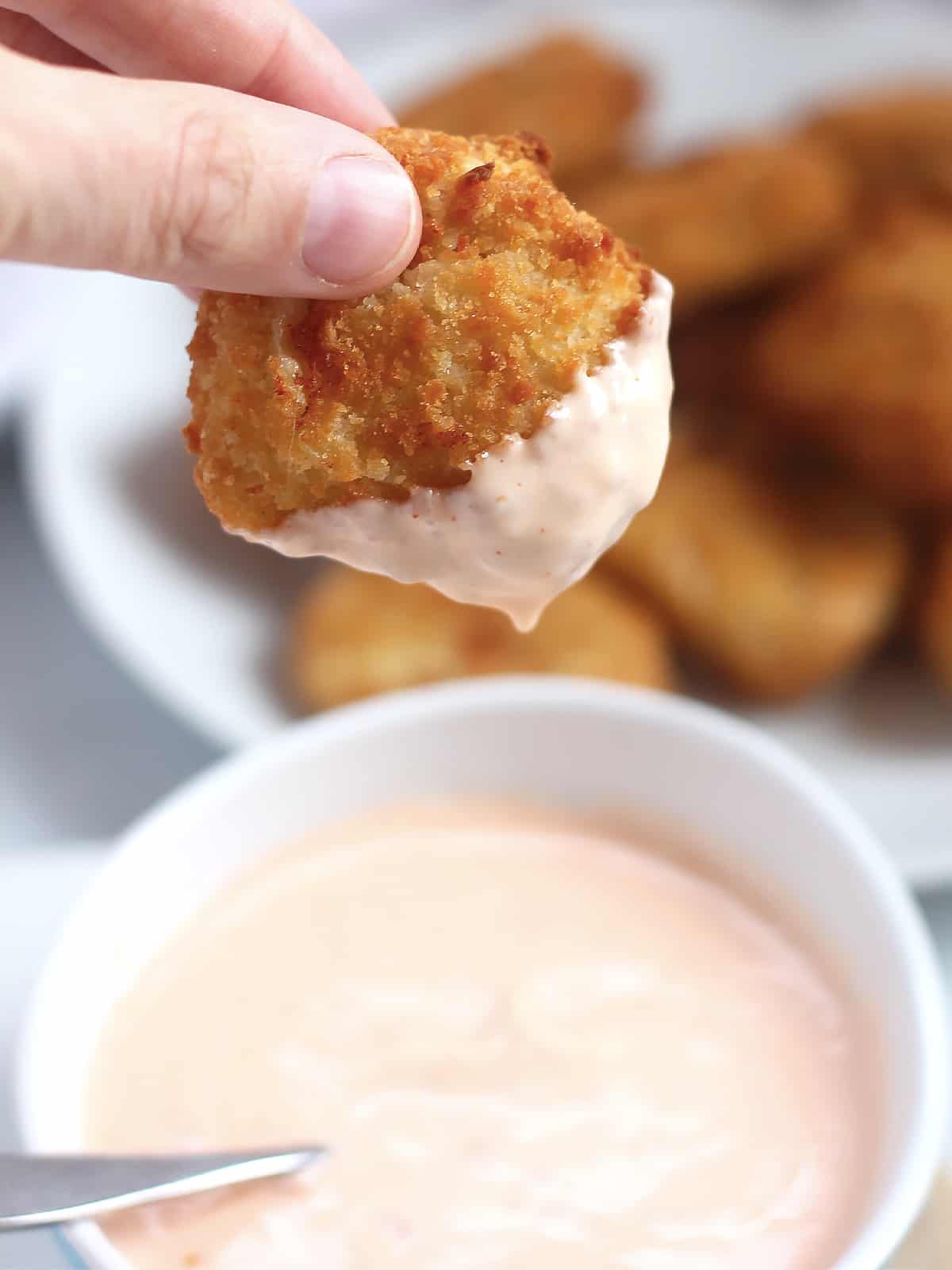 A chicken nugget being dipped into a sauce.