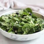 Fresh baby spinach tossed with feta and blueberries in a white bowl.