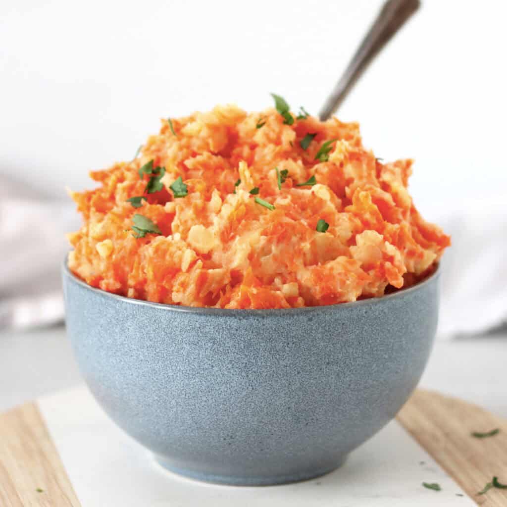 Carrot and potato mash in a blue bowl with a serving spoon.